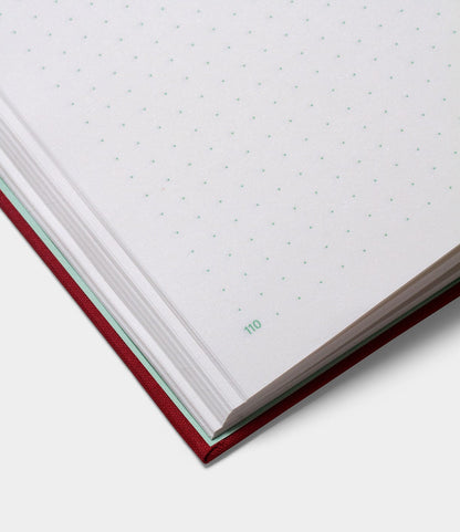 Close-up of the S.B.T. Max Cloth-Bound Notebook by Best Made Co., a red hardcover with white dotted grid pages; corner of page 110 is numbered in green.