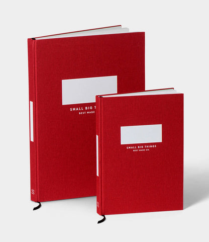 Two red S.B.T. Max Cloth-Bound Notebooks by Best Made Co. of different sizes stand upright, each hardcover with a white label and white text. The background is plain and light-colored.