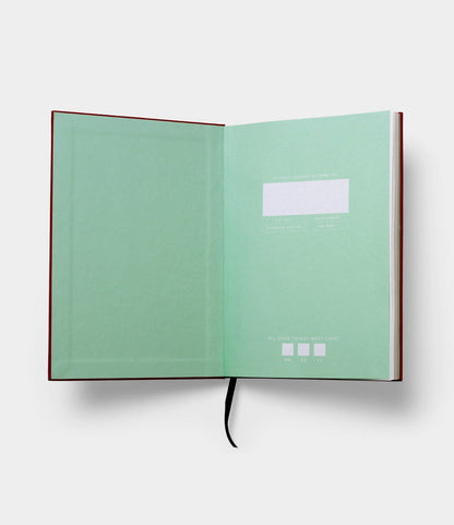 The S.B.T. Mid Cloth-Bound Notebook by Best Made Co. features an open design with a green inside cover, blank white name label, and black ribbon bookmark, all set against a plain white background.