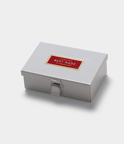 The Best Made Co. Type 6 Strongbox, Re-Founder's Edition, is a small, rectangular light gray metal box with a front latch and a red-gold "Best Made" label on the lid, perfect for organizing workshops. Shown on a plain white background.